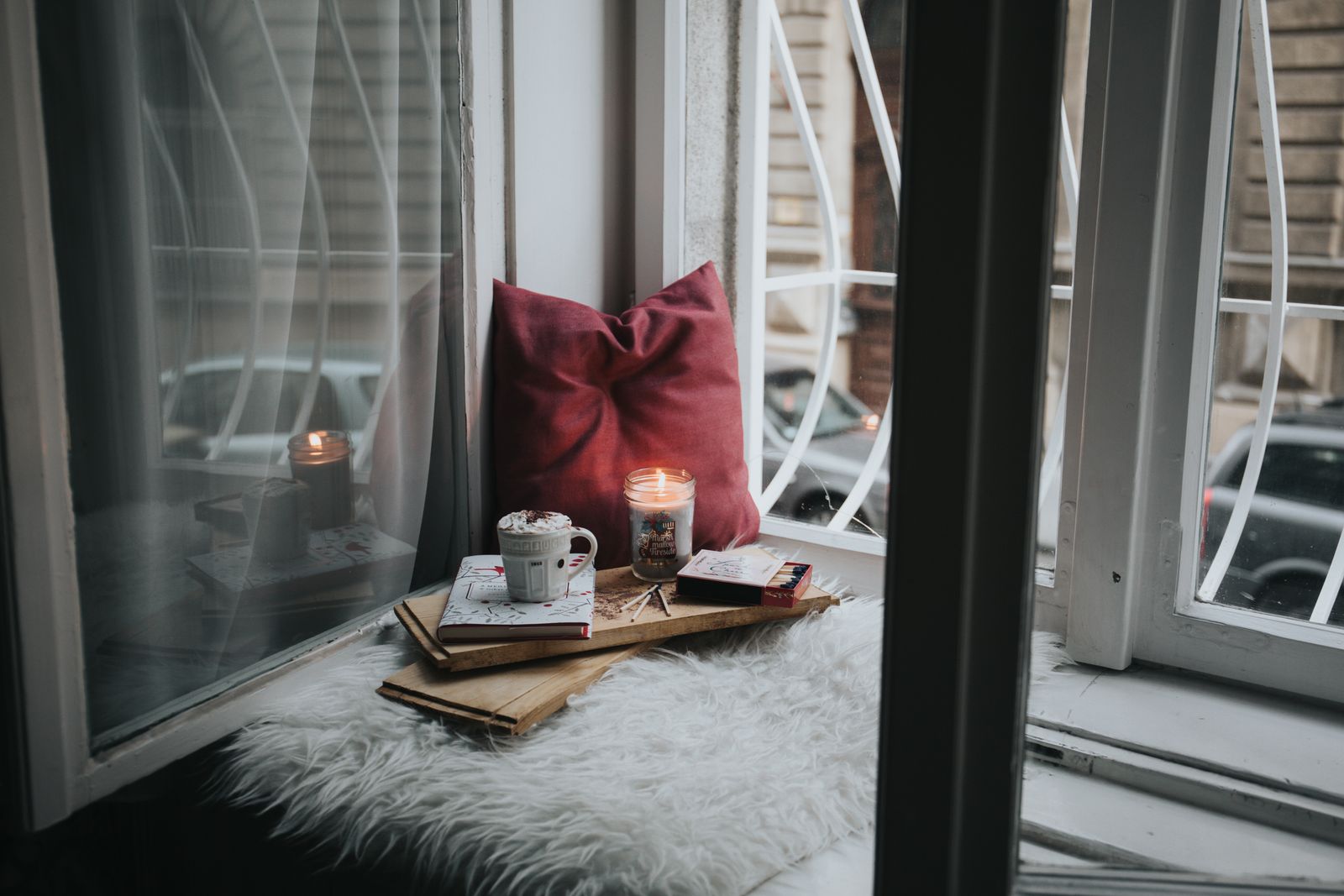 Window sill with a red pillow, a candle, and a mug on top of a book